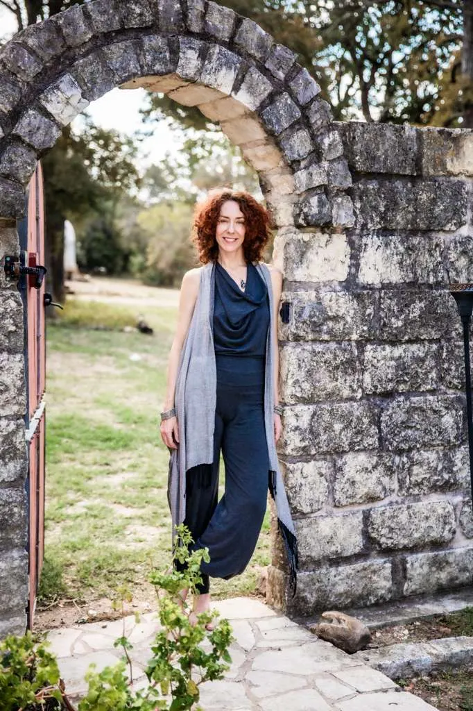 Maria standing in a stone archway, the red door open beside her